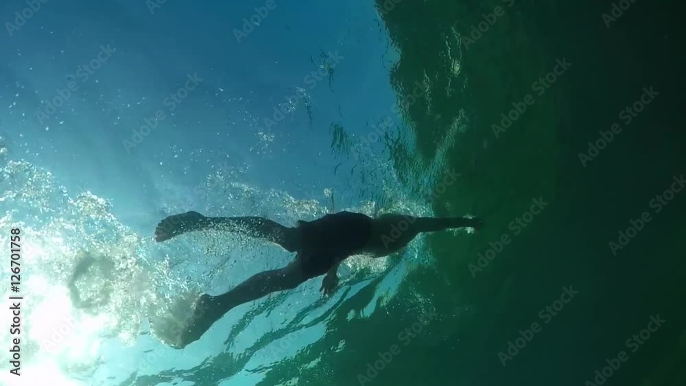 UNDERWATER LOW ANGLE: Fit man swimming above rocky coral seabed in emerald sea