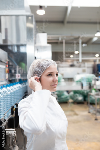 Portrait of female worker in protective working wear, standing in front of huge line for water bottling.