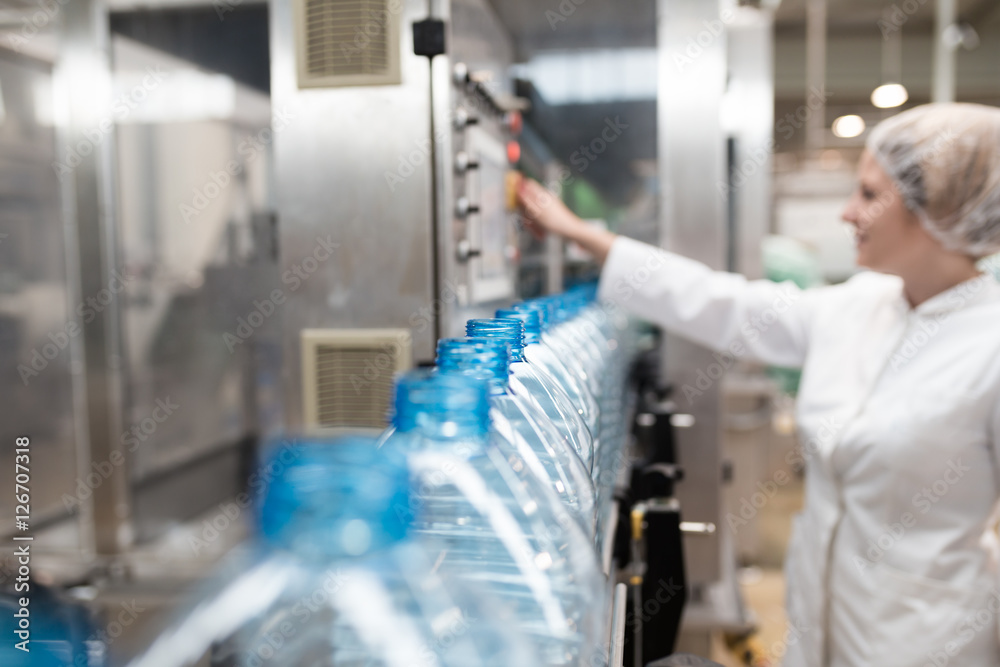 Female worker in factory checking robotic line for water bottling and packing. Inspection of quality control. Female worker in factory checking robotic line for water bottling and packing. Inspection of quality control.