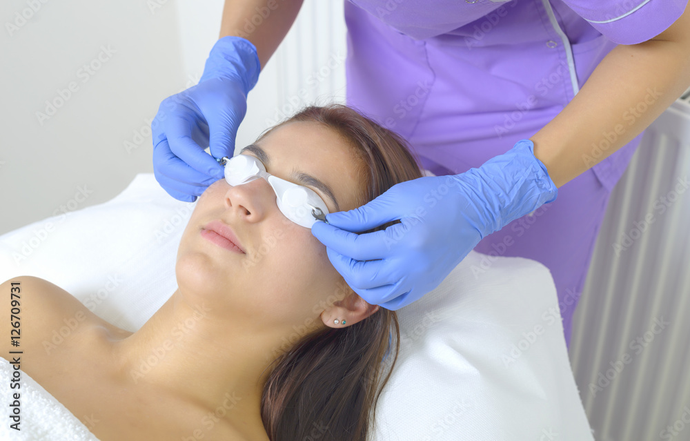 Woman lying on a table with protect glasses on eyes getting a laser skin treatment Woman lying on a table with protect glasses on eyes getting a laser skin treatment