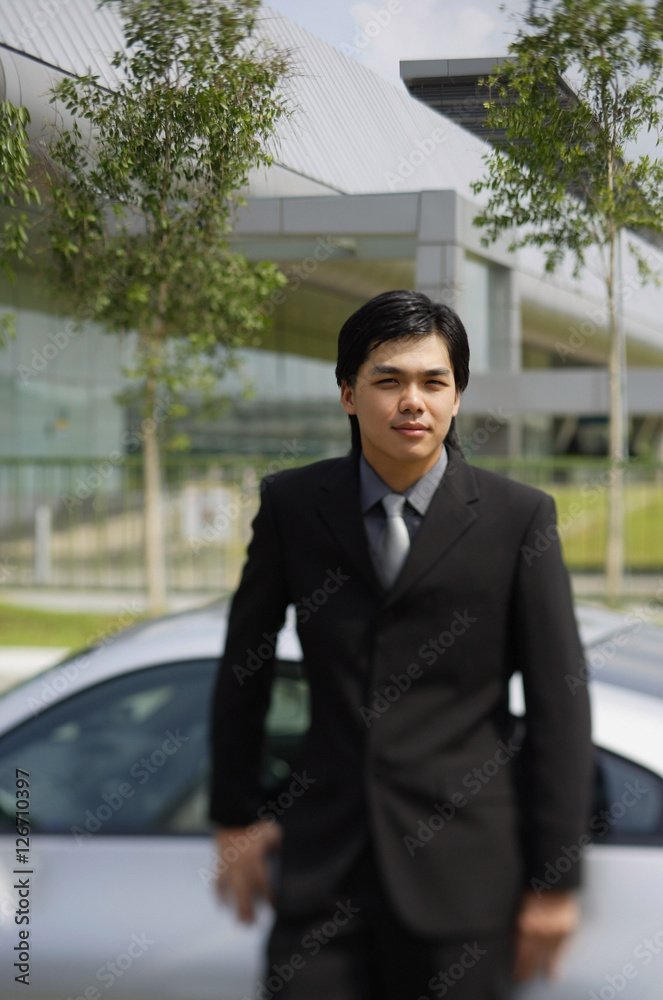 Businessman leaning on car, looking at camera Businessman leaning on car, looking at camera