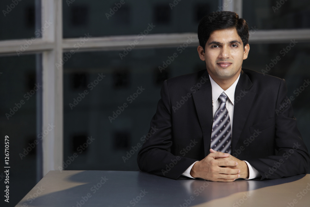 Fototapeta premium Young man sitting at table hands folded