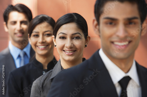 businessman in foreground  three colleagues in background  all smiling and looking at camera