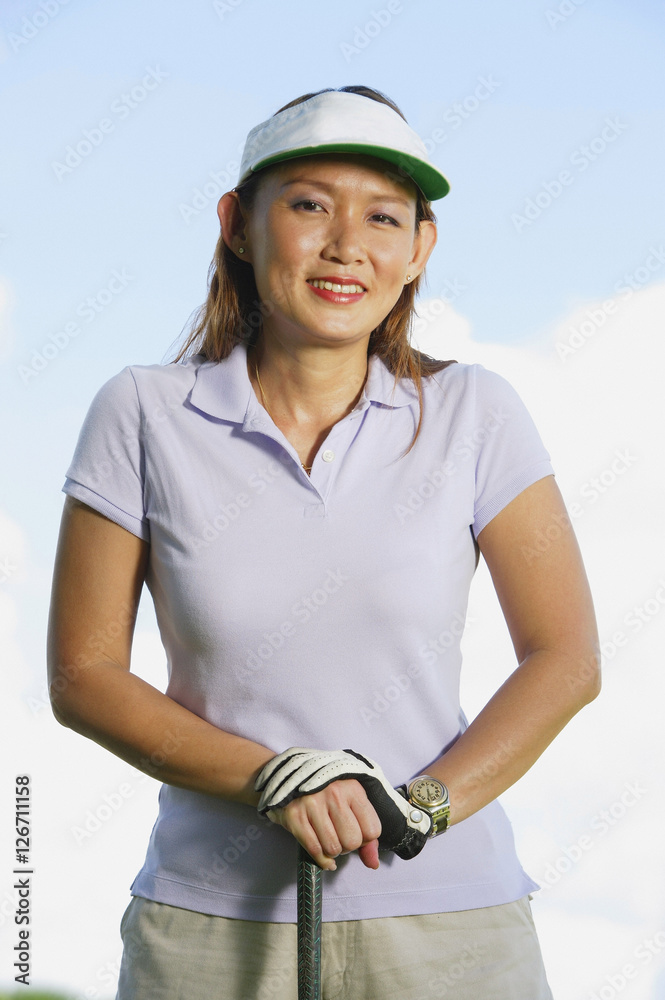 Woman wearing sun visor, leaning on golf club