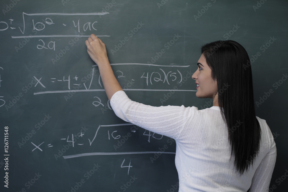 Rear view of young woman writing math equation on chalk board Rear view of young woman writing math equation on chalk board