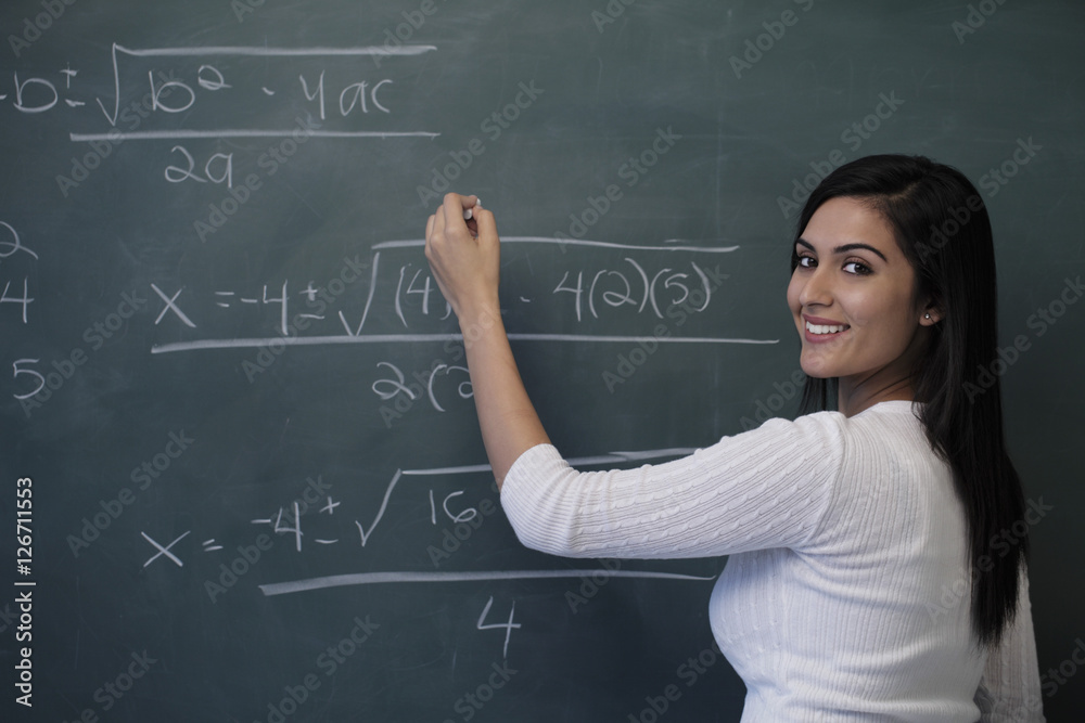 Young woman writing math equation on chalk board and smiling