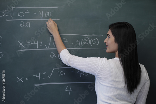 Rear view of young woman writing math equation on chalk board