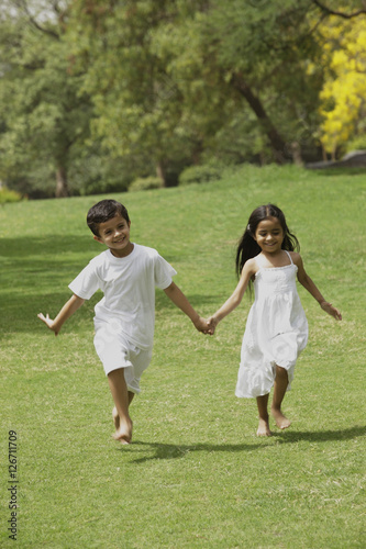 two little children running through a park holding hands