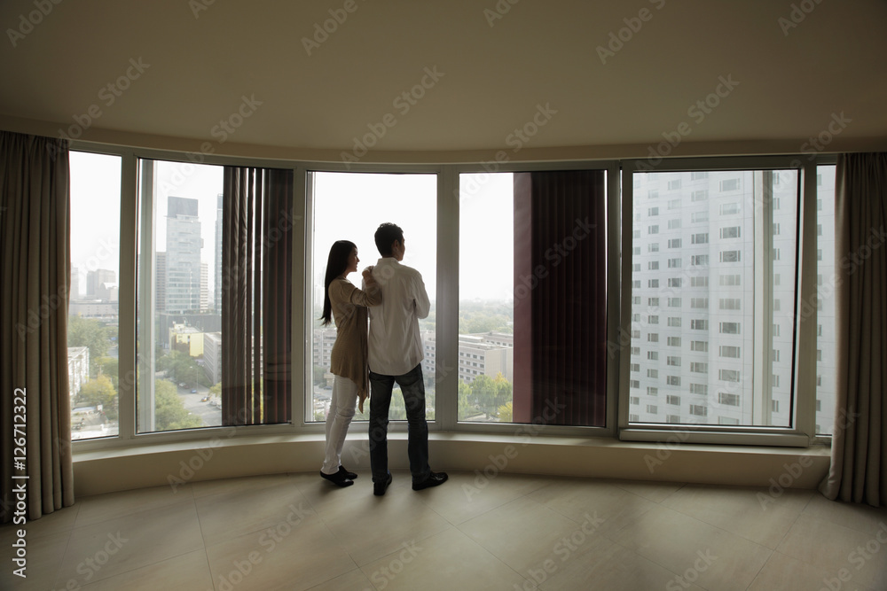 Rear view of young couple looking out large windows of condo