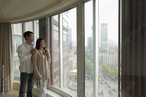 Obraz na płótnie Young couple looking out large windows at view w salonie