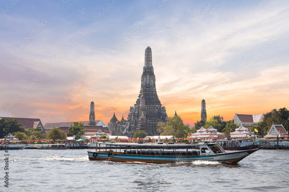 The Temple of Dawn, Wat Arun, on the Chao Phraya river with passenger ships or boat and a beautiful sky in twilight time at Bangkok, Thailand