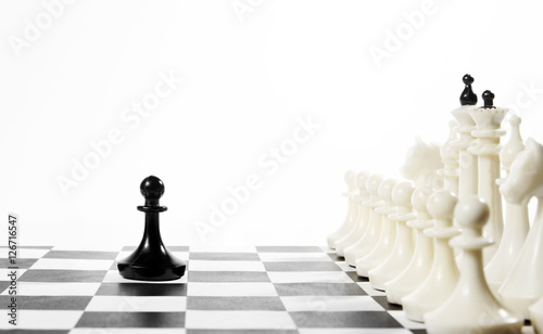 Lonely black pawn in front of enemy team. Courage and boldness. Concept with chess pieces against white background