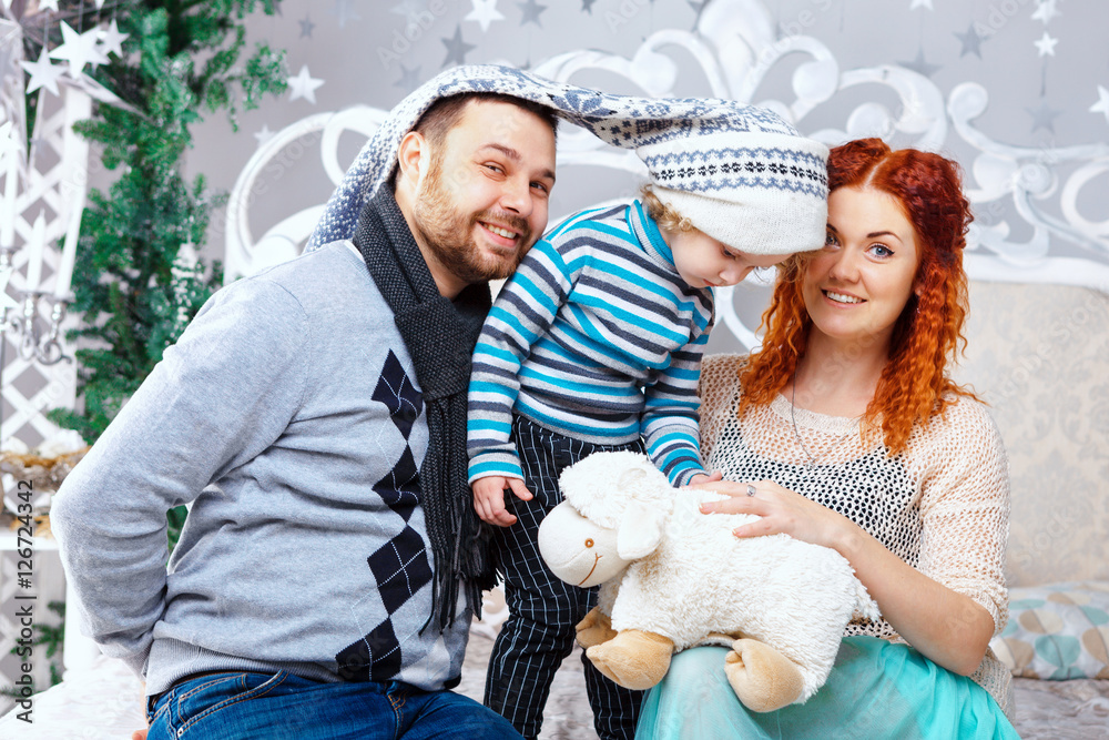 Christmas happy family of three persons and fir tree with gift boxes over white bedroom background Christmas happy family of three persons and fir tree with gift boxes over white bedroom background