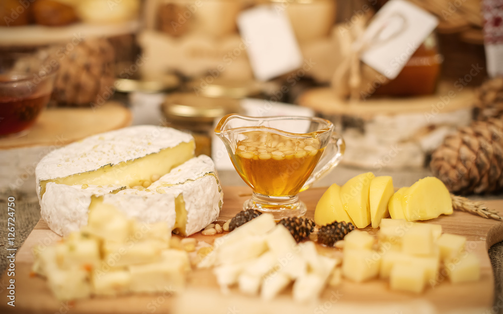 different cheeses and cedar nuts amount liquid honey on wooden t