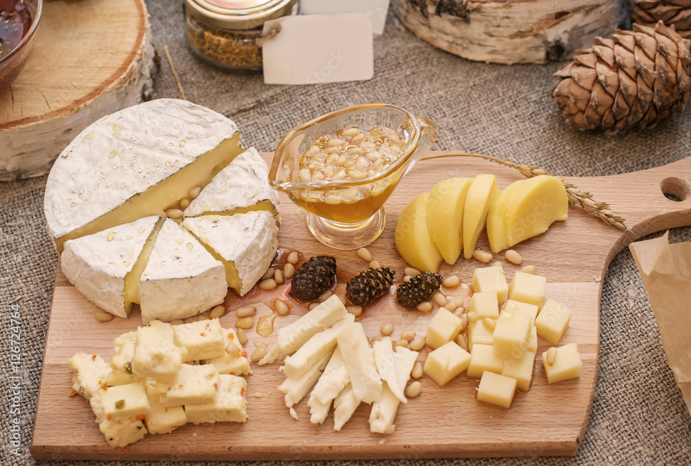 different cheeses and cedar nuts amount liquid honey on wooden t