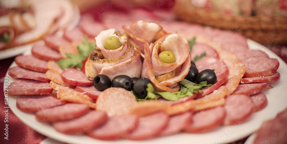 slices of ham, sausages and salami with olives decorated on plat
