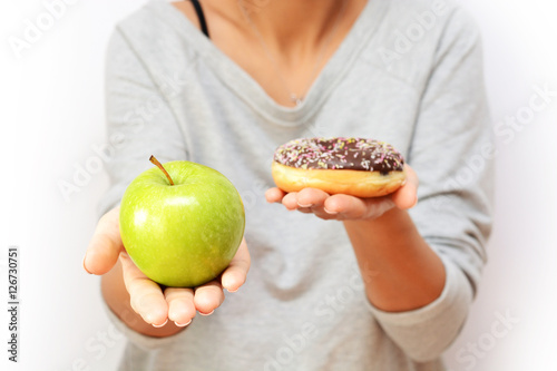 Healthy lifestyle or nutrition concept with young woman holding in hands an green apple and a donut
