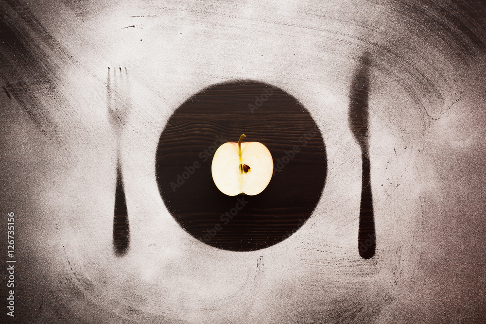 Obraz premium Half of apple on the silhouette plate, knife and fork.