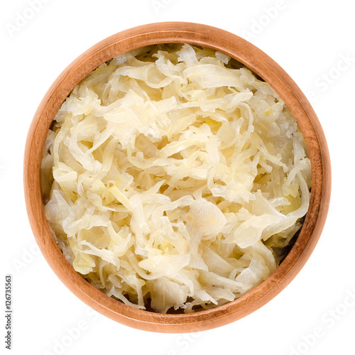 German sauerkraut in wooden bowl over white. Finely cut cabbage, fermented by lactic acid bacteria with long shelf life and distinctive sour flavor, used as a side dish. Isolated macro food photo.