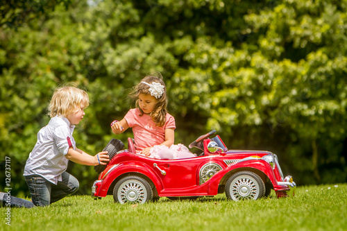 young happy children - boy and girl - driving a toy car outdoors