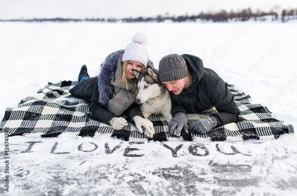 portrait of a young couple with dog lying on snow.