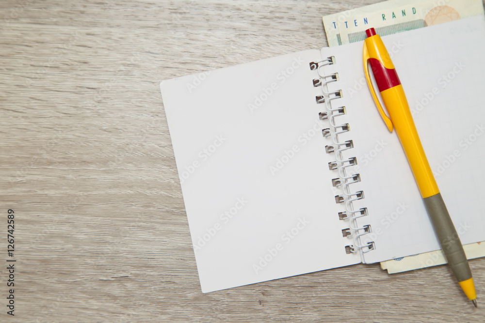 Blank notebook page and pen with South African Rand on wooden office table Blank notebook page and pen with South African Rand on wooden office table