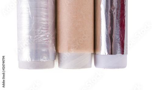 One roll of plastic wrap, one roll of aluminum foil and One roll of parchment paper for household use on a light background. Isolation.