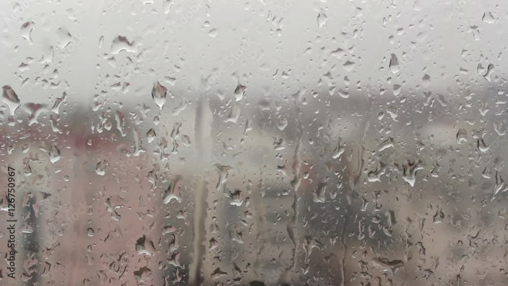 Raindrops falling down at home window; city panorama visible in background; focus on front plane