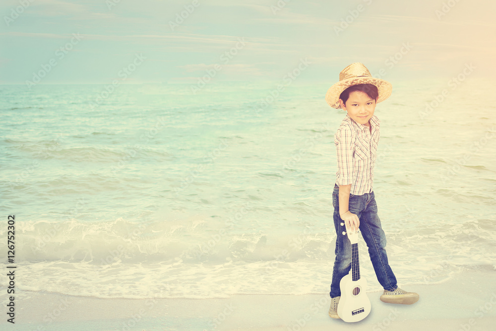 Seven years old Asian boy is standing with ukulele at beach happily