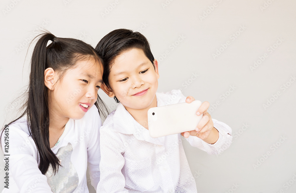 Lovely Asian couple school kids are taking selfie, 7 and 10 years old, over gray background Lovely Asian couple school kids are taking selfie, 7 and 10 years old, over gray background