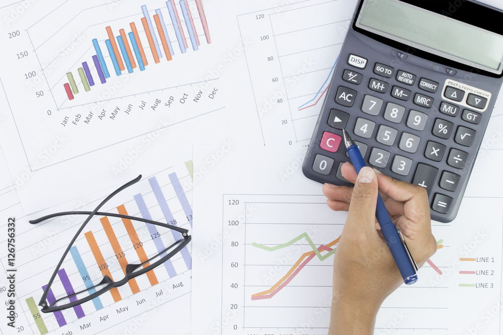 business concept : glasses and calculator with hand holding pen on stock market report as background business concept : glasses and calculator with hand holding pen on stock market report as background