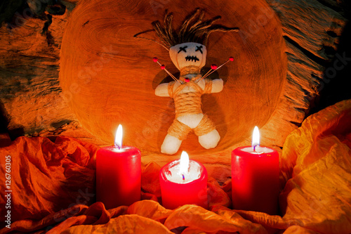A voodoo doll with needles stands on an altar with candles
