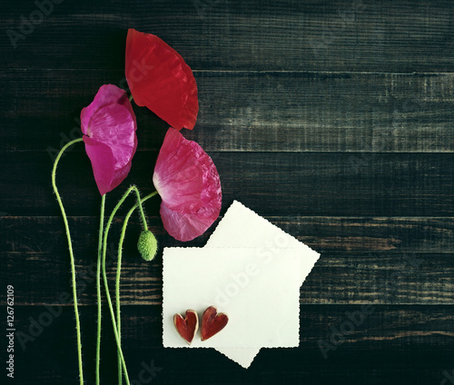 Red and pink poppys and white card with the inscription and two decorative hearts on an old textural wooden surface photo
