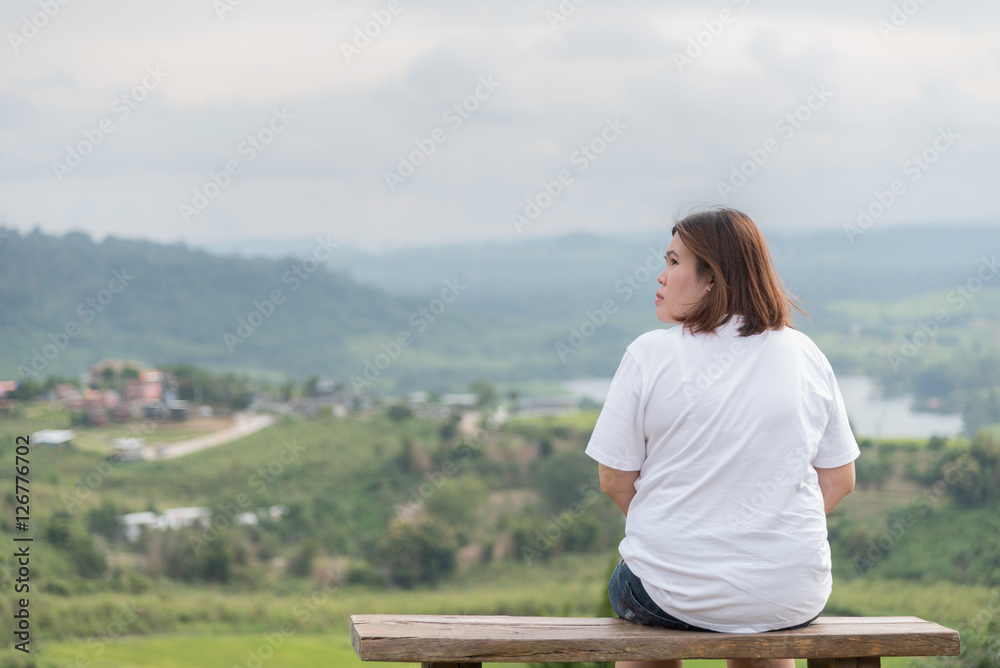 The view from behind young woman sitting on the hilltop.