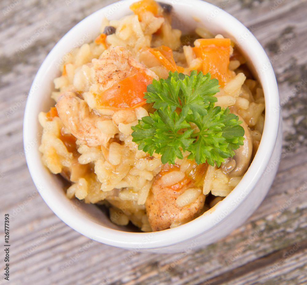 Risotto with chicken, bell pepper, onion, portobello and parsley on a wooden background Risotto with chicken, bell pepper, onion, portobello and parsley on a wooden background