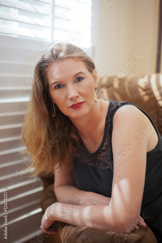 Mature Blonde Female Leaning on Chairs Arm Looking at Camera