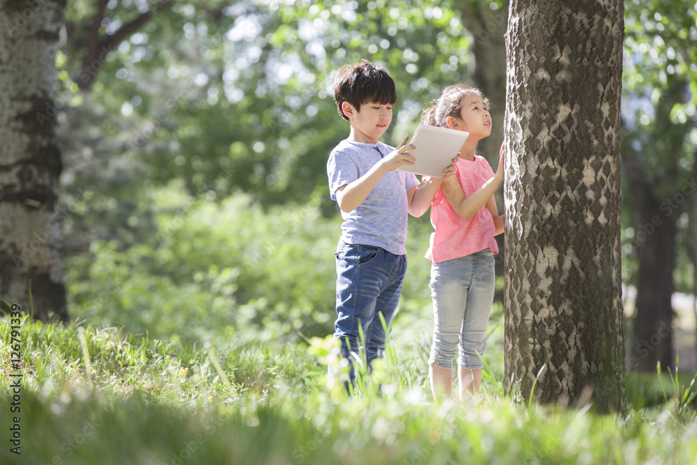 Children with digital tablet looking at tree trunk Children with digital tablet looking at tree trunk