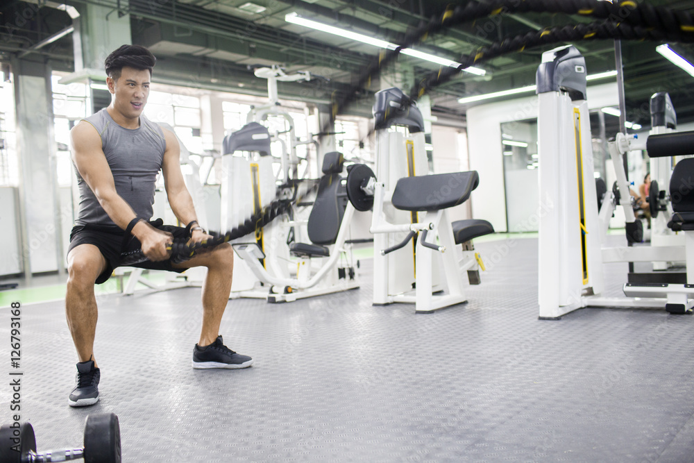 Young man exercising with battling rope at gym Young man exercising with battling rope at gym
