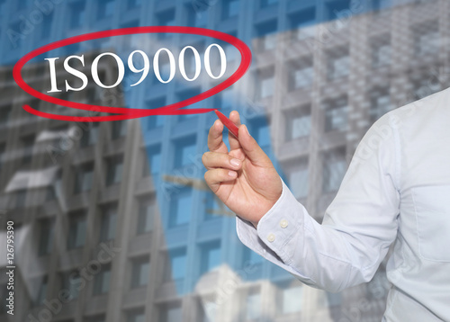 Hand of young businessman write the word ISO 9000 on skyscrapers photo