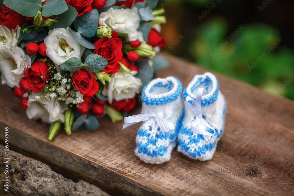 Wedding bouquet of roses and baby booties on wooden background