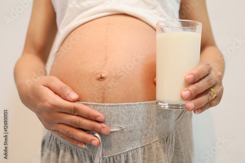 Pregnant women hold milk glass of drink in hand placed on belly.