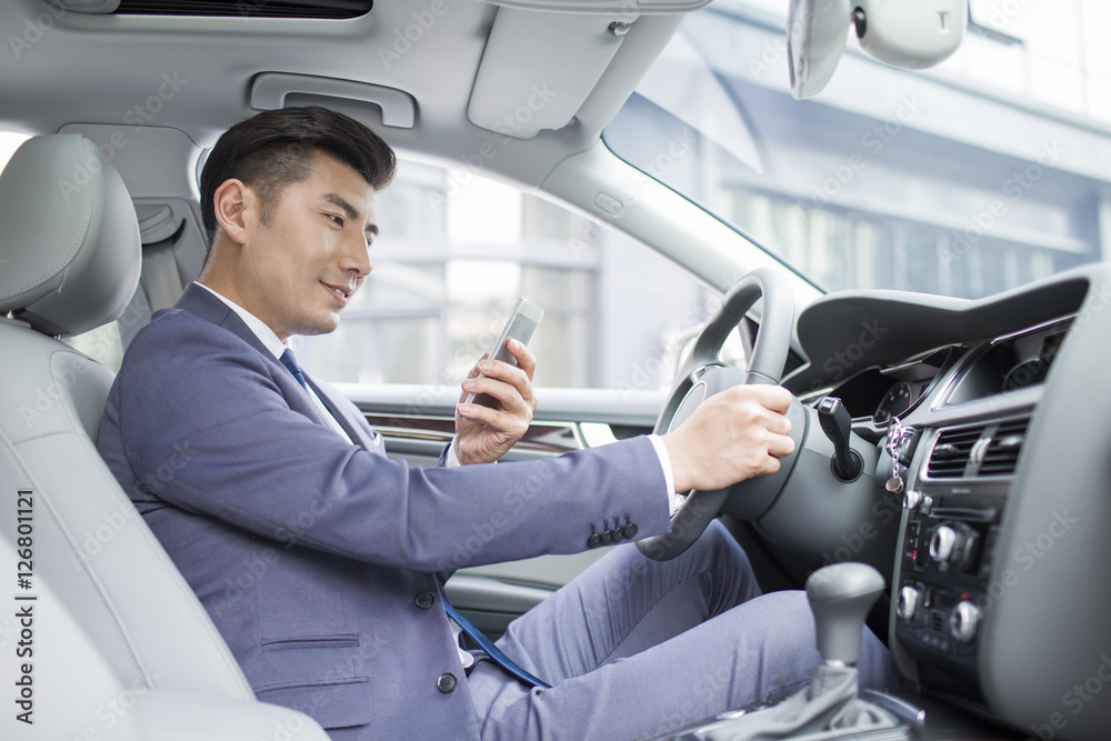 Confident businessman holding smart phone in a car Confident businessman holding smart phone in a car