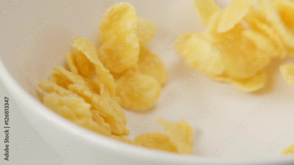 SLOW MOTION: Corn flakes fall on white dish (close up) SLOW MOTION: Corn flakes fall on white dish (close up)