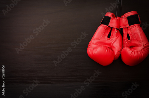 Two red boxing gloves hanging on a black background in the corner of the frame, place for text