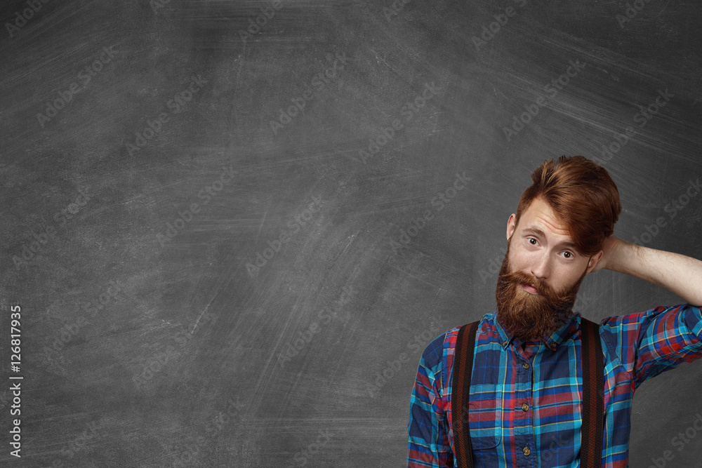 Human face expressions and emotions. Doubtful and surprised bearded man dressed in checkered shirt looking confused and puzzled, raising his brows in surprise and indignation, scratching his head
