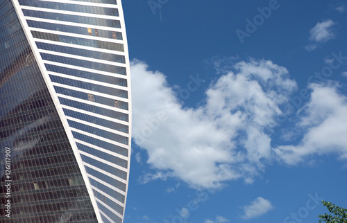 View of high modern spiral office tower building of glass and metal over blue sky with clouds in sunny day