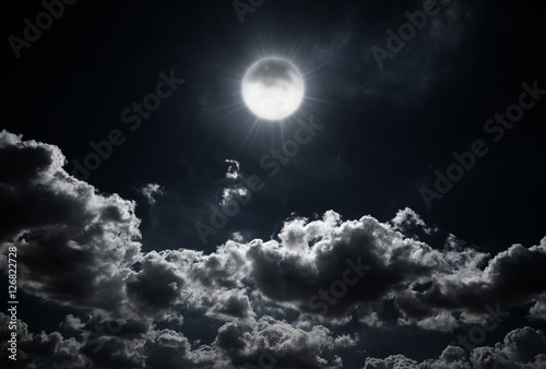 Dramatic photo illustration of a nighttime sky with brightly lit clouds and large. Beautiful starry night sky with clouds and bright full moon or super moon.