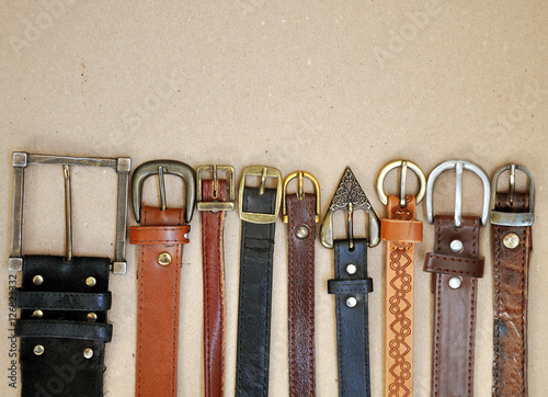 Fashion background. Vintage brown leather belts with metal rusty buckle on beige cardboard surface closeup.
