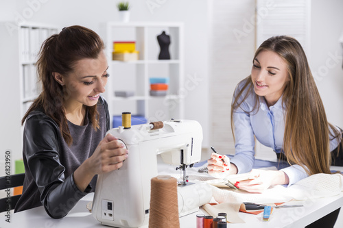 Girl is sewing. Her colleague is smiling