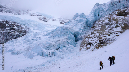 a mountain guide and clients below a glacier in the Swiss Alps on a backcountry ski excursion